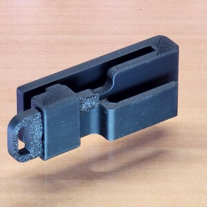 May include: A black plastic key holder with a loop for attaching to a keychain. The holder has a slot for holding a key.