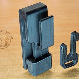 May include: A black plastic 3D printed phone holder with a separate black plastic hook. The holder has a textured surface and a slot for a phone.
