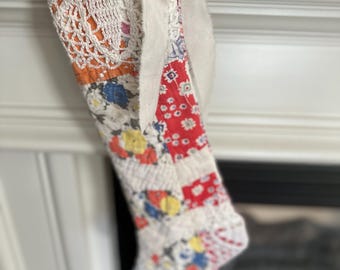 May include: A patchwork Christmas stocking with a white crocheted top and a white fabric bow. The stocking is made of various fabrics with red, blue, and yellow patterns.