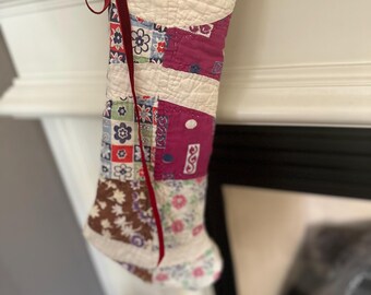 May include: A patchwork Christmas stocking with a red velvet ribbon. The stocking is made of various fabrics with floral patterns in shades of pink, blue, and green.
