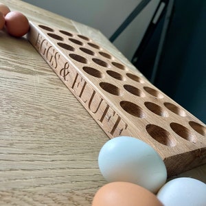 May include: A wooden egg holder with 24 slots, labeled "EGGS & FLUFFE". Three white eggs are in the foreground.
