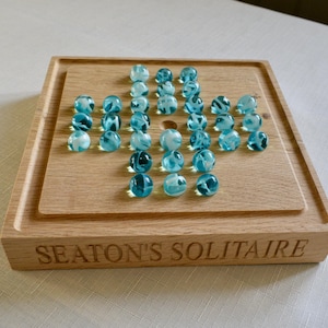 Peut inclure: Un plateau de jeu en bois avec les mots "Seaton's Solitaire" gravés sur le devant. Le plateau a un motif de grille avec 37 billes bleues en place.