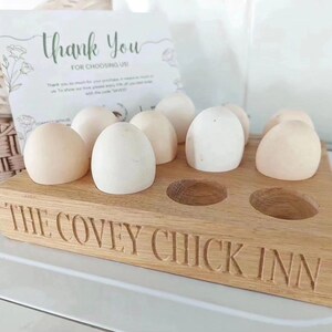 May include: Wooden egg holder with the text "The Covey Chick Inn" engraved on the front. The holder has six slots and is filled with six white eggs.