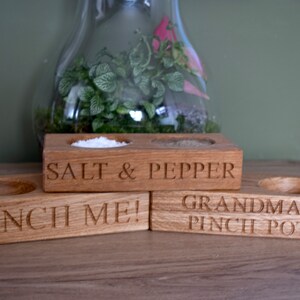May include: Three wooden salt and pepper shakers with engraved text. The first shaker says "Salt & Pepper", the second says "Pinch Me!" and the third says "Grandma's Pinch Pot".