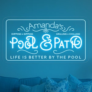 Könnte beinhalten: Blaues Wohnzimmer mit Neon-Schild "Amanda's Pool & Patio". Unter dem Schild befindet sich ein blaues Sofa mit Kissen. Ein weißer Couchtisch mit einer Vase mit weißen Blumen und einem geflochtenen Tablett. Entspannte Atmosphäre.