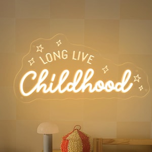 Könnte beinhalten: Ein Kinderzimmer mit einem Neon-Schild mit der Aufschrift "LONG LIVE Childhood". Der Raum umfasst einen gelben Schrank, ein Bücherregal aus Holz mit Büchern, ein Bett mit einem sternförmigen Kissen und eine kleine Lampe.