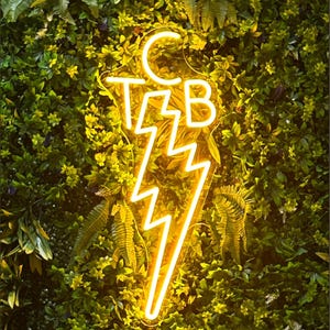 Puede incluir: Un letrero de neón amarillo con un diseño de rayo y las letras "C.T.B." dentro del rayo.