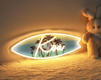 Puede incluir: Un letrero de neón blanco con forma de tabla de surf con palmeras y el nombre "Koa" en letra cursiva. El letrero está encendido y brillando.