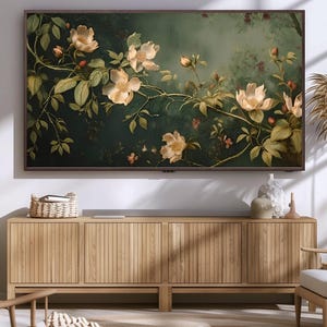 May include: A wooden cabinet with three doors, each with vertical slats, sits in front of a wall with a framed painting of white flowers on a dark green background. The cabinet is made of light wood and has a natural finish.