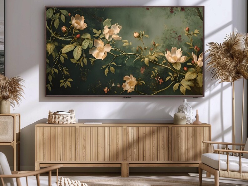 May include: A wooden cabinet with three doors, each with vertical slats, sits in front of a wall with a framed painting of white flowers on a dark green background. The cabinet is made of light wood and has a natural finish.