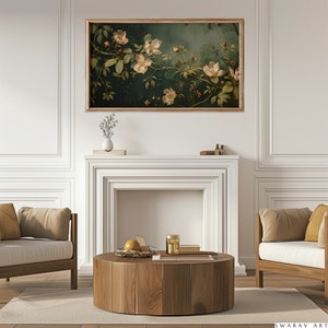 May include: A framed painting of white flowers with green leaves on a dark green background. The painting is hanging above a white fireplace mantel with a wooden coffee table in front of it.
