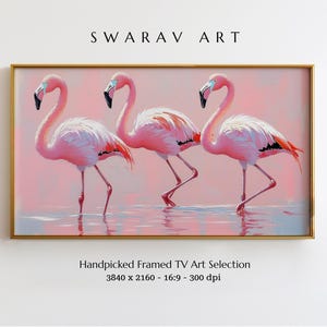 May include: Framed artwork featuring three pink flamingos standing in water. The birds have black beaks and red accents on their wings. The background is a soft pink, and the artwork is in a gold frame. The text "SWARAV ART" is at the top.