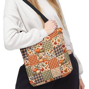 Op de afbeelding: Een draagtas met een patchworkontwerp met afwisselende vierkanten in oranje, groene en blauwe ruitpatronen, afgewisseld met illustraties van pompoenen, herfstbladeren en kleine bloemen op een crèmekleurige achtergrond met zwarte hengsels.