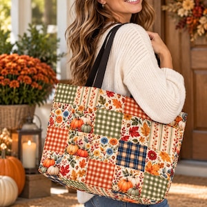 May include: A tote bag featuring a patchwork design with various autumn-themed patterns including orange pumpkins, colourful fall leaves, and plaid squares in shades of green, orange, and blue. The bag has two black shoulder straps.