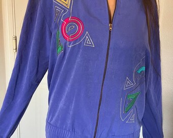 May include: A purple bomber jacket with a colorful geometric design embroidered on the front. The jacket has a zipper closure and a ribbed hem and cuffs.