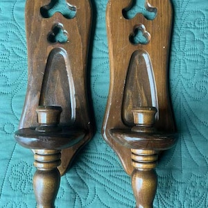 May include: A pair of wooden wall sconces with a dark brown finish. Each sconce has a carved design and a candle holder.
