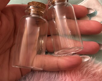 May include: Two clear glass bottles with cork stoppers. The bottles are empty and have a round shape.