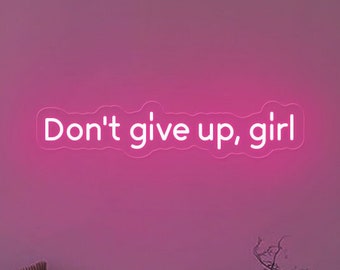 Puede incluir: Un letrero de neón rosa con el texto "Don't give up, girl" en una pared rosa. El letrero está colgado sobre un sofá con almohadas y una pequeña planta.