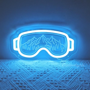 May include: A neon sign shaped like a pair of ski goggles with a mountain scene inside. The neon is a bright blue colour.