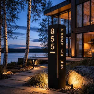 May include: A tall, rectangular, black metal address post featuring illuminated cut-out lettering that displays the number 855 and the text PARKVIEW WAY in a vertical orientation, glowing with a warm yellow light against the dark exterior.
