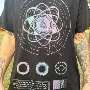 May include: Black t-shirt with a graphic design of a stylized atom with a circle in the center. The atom is surrounded by a series of concentric circles with text in a circular pattern. The text reads "Surely in time, ye are one with the Master. Surely by right, ye are one with the Master. Surely by right, ye are one with the ALL."