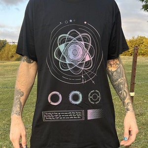 May include: Black t-shirt with a graphic print of a stylized atom with a circular design and the text "Surely in live, ye are ane with the Yaster. Surely by right ye are ane with the Yer. Surely by right, ye are ane with the ALL."