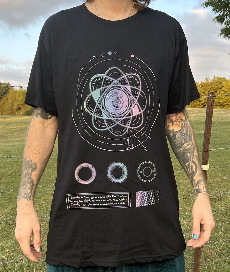 May include: Black t-shirt with a graphic print of a stylized atom with a circular design and the text "Surely in live, ye are ane with the Yaster. Surely by right ye are ane with the Yer. Surely by right, ye are ane with the ALL."