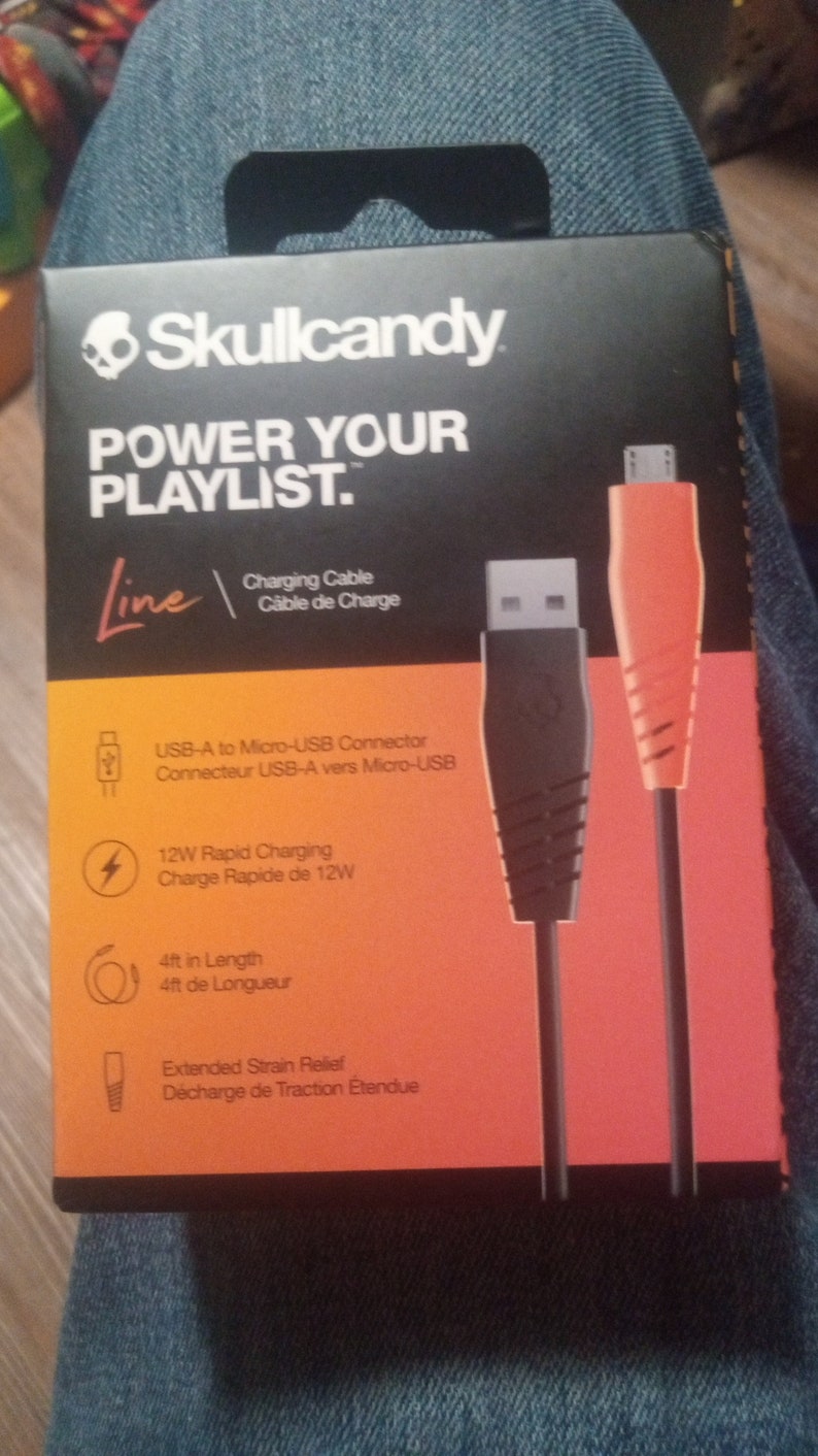 Może przedstawiać: Czarno-pomarańczowe opakowanie kabla ładującego Skullcandy. Opakowanie zawiera tekst &bdquo;POWER YOUR PLAYLIST&rdquo; oraz szczeg&oacute;ły dotyczące złącza USB-A do Micro-USB, szybkiego ładowania 12 W i długości 1,22 m.