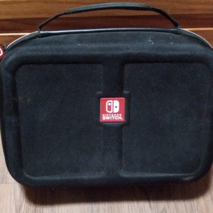 May include: Black Nintendo Switch carrying case with a red Nintendo Switch logo. The case has a zipper closure and a handle.