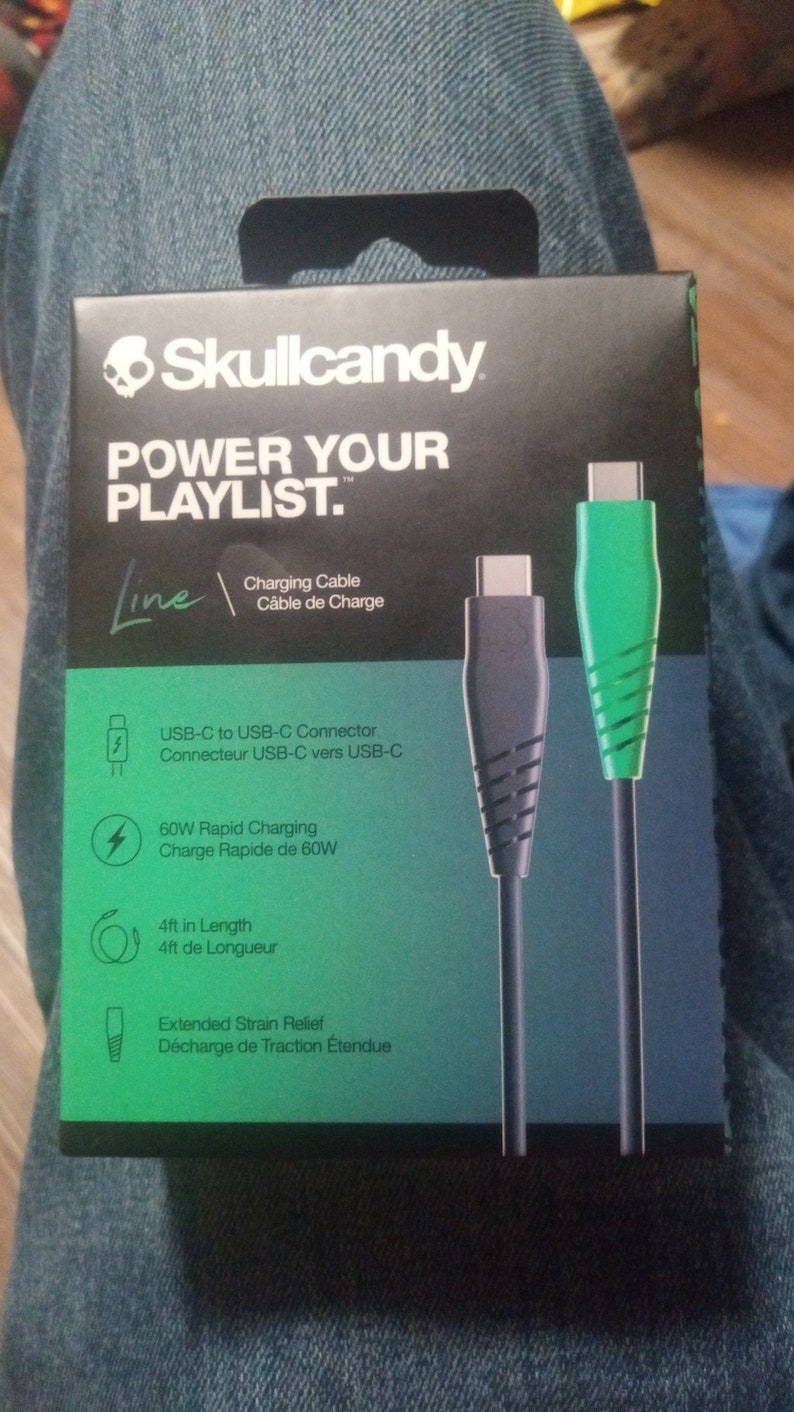 Może przedstawiać: Czarno-zielone pudełko kabla ładującego Skullcandy. Na pudełku widnieje napis "POWER YOUR PLAYLIST." oraz szczeg&oacute;ły dotyczące złącza USB-C do USB-C, szybkiego ładowania 60W i długości 1,2 m.