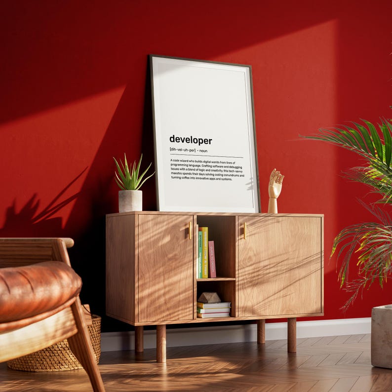 May include: A wooden cabinet with a framed print defining "developer". The print is in a black frame and features the word "developer" at the top. A small potted plant and a wooden hand sculpture are also on the cabinet.