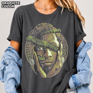 May include: A graphite-coloured t-shirt featuring a graphic print of a person's face partially obscured by a green snake. The design is framed by a circular Greek key border. The text GRAPHITE COLOR is printed in the upper left corner of the image.