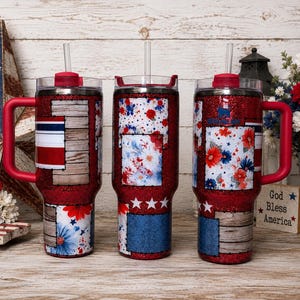 May include: Three red glitter tumblers with handles and clear straws. Each features a patchwork design of wood grain, red and blue floral patterns, and white stars. The tumblers have clear lids with red accents and are displayed on a wooden surface.