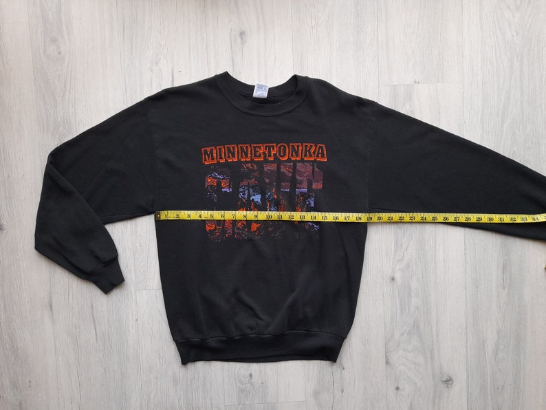 May include: Black long-sleeve sweatshirt with a graphic print of "Minnetonka" in orange and red letters. The graphic is made up of small images of buildings and trees.