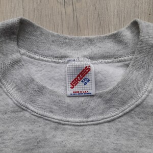 May include: Gray sweatshirt with a Jerzees tag. The tag is red and white and says "Jerzees" in a black font. The tag also says "XXL 48-50" and "Made in U.S.A."