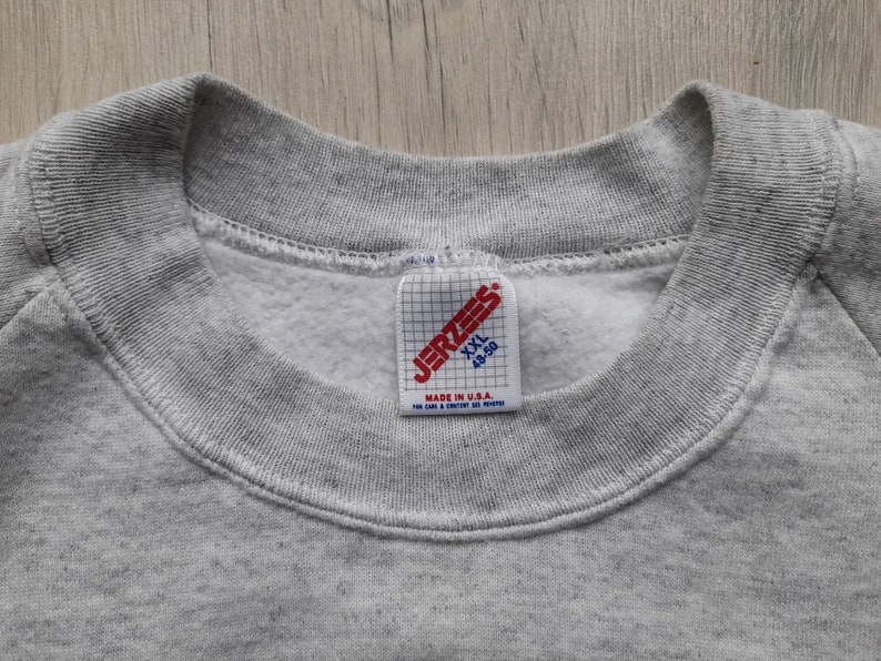 May include: Gray sweatshirt with a Jerzees tag. The tag is red and white and says "Jerzees" in a black font. The tag also says "XXL 48-50" and "Made in U.S.A."