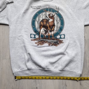 May include: Gray sweatshirt with a graphic print of a deer in a forest setting. The graphic includes the text "Brown County State Park".