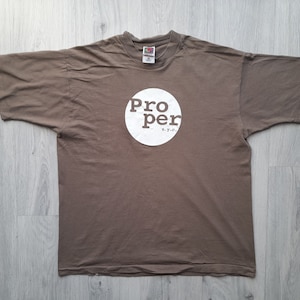 May include: A brown t-shirt with a white circle logo that says "Pro per" in a vintage style font. The logo also includes the text "n.y.c."