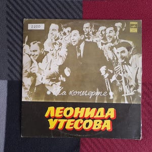 Puede incluir: Una portada de disco de vinilo vintage con una foto en blanco y negro de un grupo de hombres con traje. La portada está titulada "Na kontserte Leonida Utesova" en escritura cirílica.