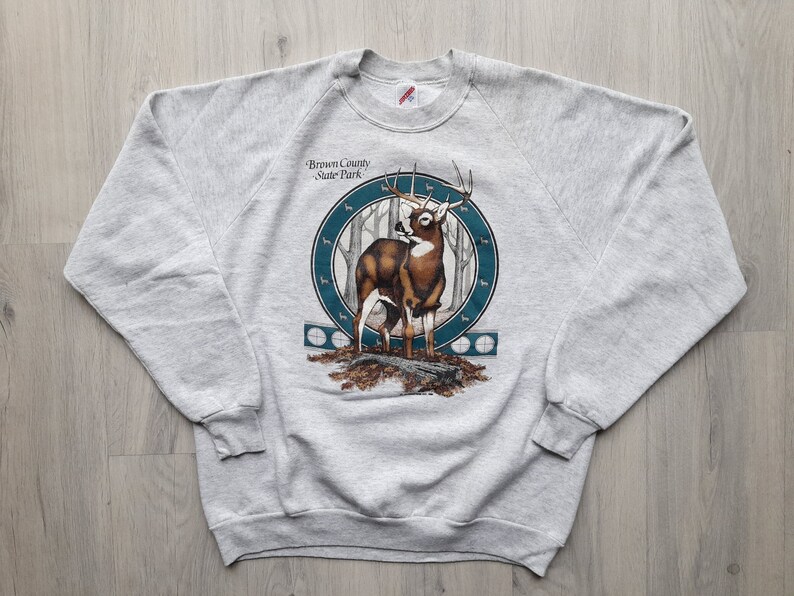 May include: Gray sweatshirt with a graphic of a white-tailed deer in a forest setting. The graphic includes the text "Brown County State Park".
