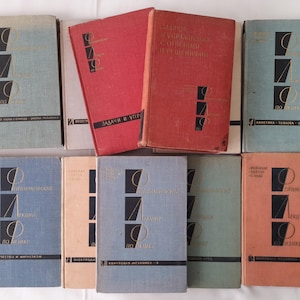 Pode incluir: Uma coleção de nove livros encadernados em azul, vermelho e verde com o título "Задачи и Упражнения по Физике" no livro vermelho. Os livros estão dispostos em três filas.