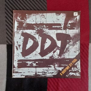 May include: Album cover featuring the band name "DDT" in large, dark brown letters against a light blue and brown background with paint splatter effects. The album title is in Russian.