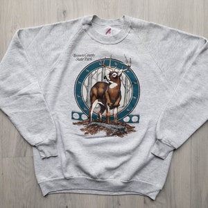 May include: Gray sweatshirt with a graphic print of a white-tailed deer in a forest setting. The text "Brown County State Park" is printed above the deer.