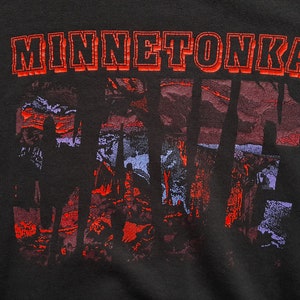 May include: Black t-shirt with a red and white graphic print of the word "MINNETONKA" and a stylized image of trees and a sunset.