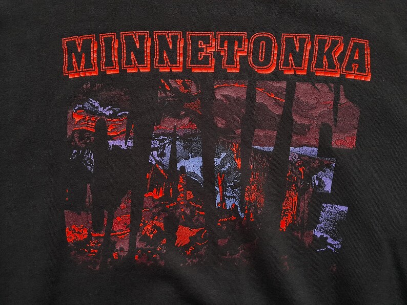 May include: Black t-shirt with a red and white graphic print of the word "MINNETONKA" and a stylized image of trees and a sunset.