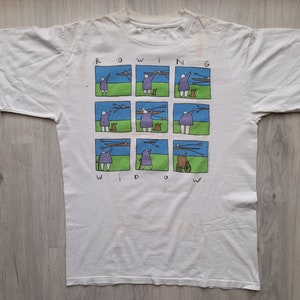 May include: White t-shirt with a cartoon illustration of a woman rowing a boat. The illustration is repeated in a grid pattern and the text "ROWING WIDOW" is printed above and below the image.
