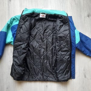 Puede incluir: Chaqueta vintage con bloques de color en tonos azules y turquesas, con forro acolchado negro. La chaqueta tiene cierre de cremallera y una peque&ntilde;a etiqueta en el cuello. Las mangas son de color azul liso.