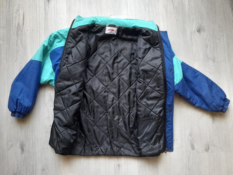 Puede incluir: Chaqueta vintage con bloques de color en tonos azules y turquesas, con forro acolchado negro. La chaqueta tiene cierre de cremallera y una peque&ntilde;a etiqueta en el cuello. Las mangas son de color azul liso.