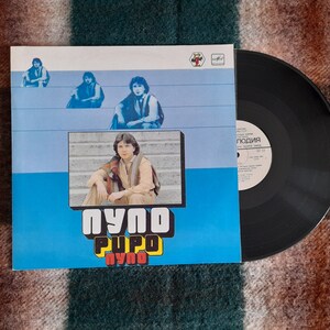 Op de afbeelding: Een vinyl platenhoes met een blauwe achtergrond en een band van drie jonge mannen. De albumtitel is "пупо пупо пупо" in rode en gele letters. Het platenlabel is "Мелодия".