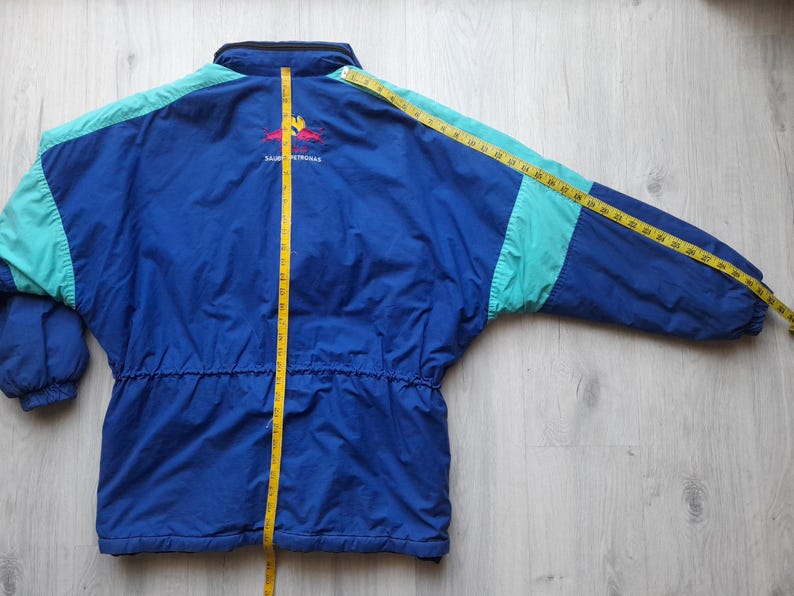 Puede incluir: Chaqueta vintage azul y turquesa con cintura con cord&oacute;n y logotipo en la espalda. La chaqueta se mide con una cinta m&eacute;trica amarilla. La chaqueta mide aproximadamente 76 cm de largo.